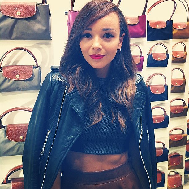 Ashley Madekwe posed in front of a colorful wall of Longchamp bags at