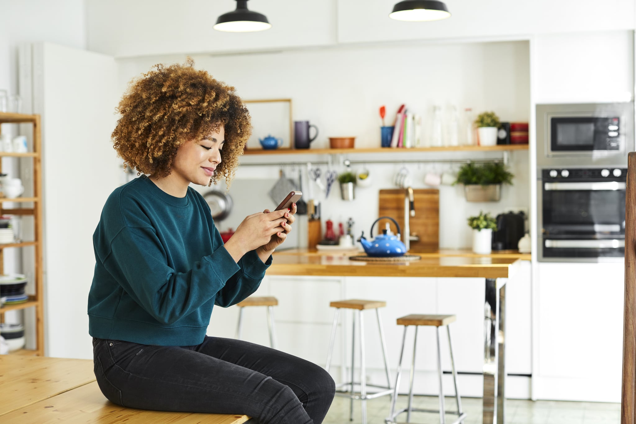 Young woman surfing social media at home. Beautiful female is using smartphone while sitting on table. She is wearing casuals.