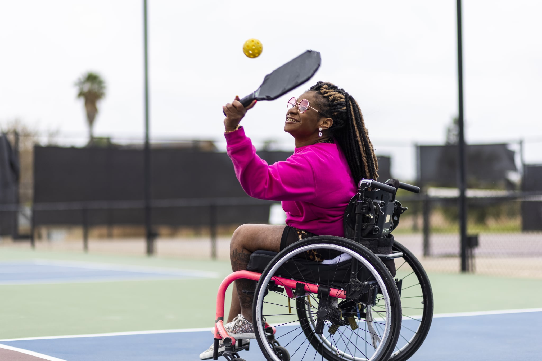 A young black disabled woman playing pickleball with her friend