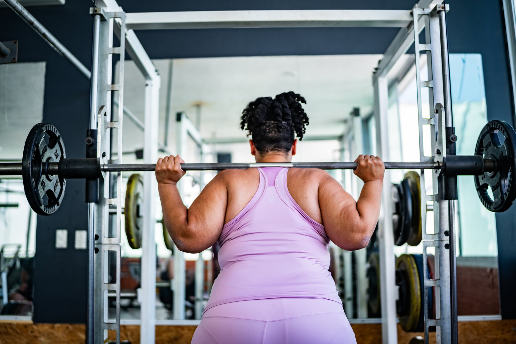 Mid adult woman doing squats with barbell at gym