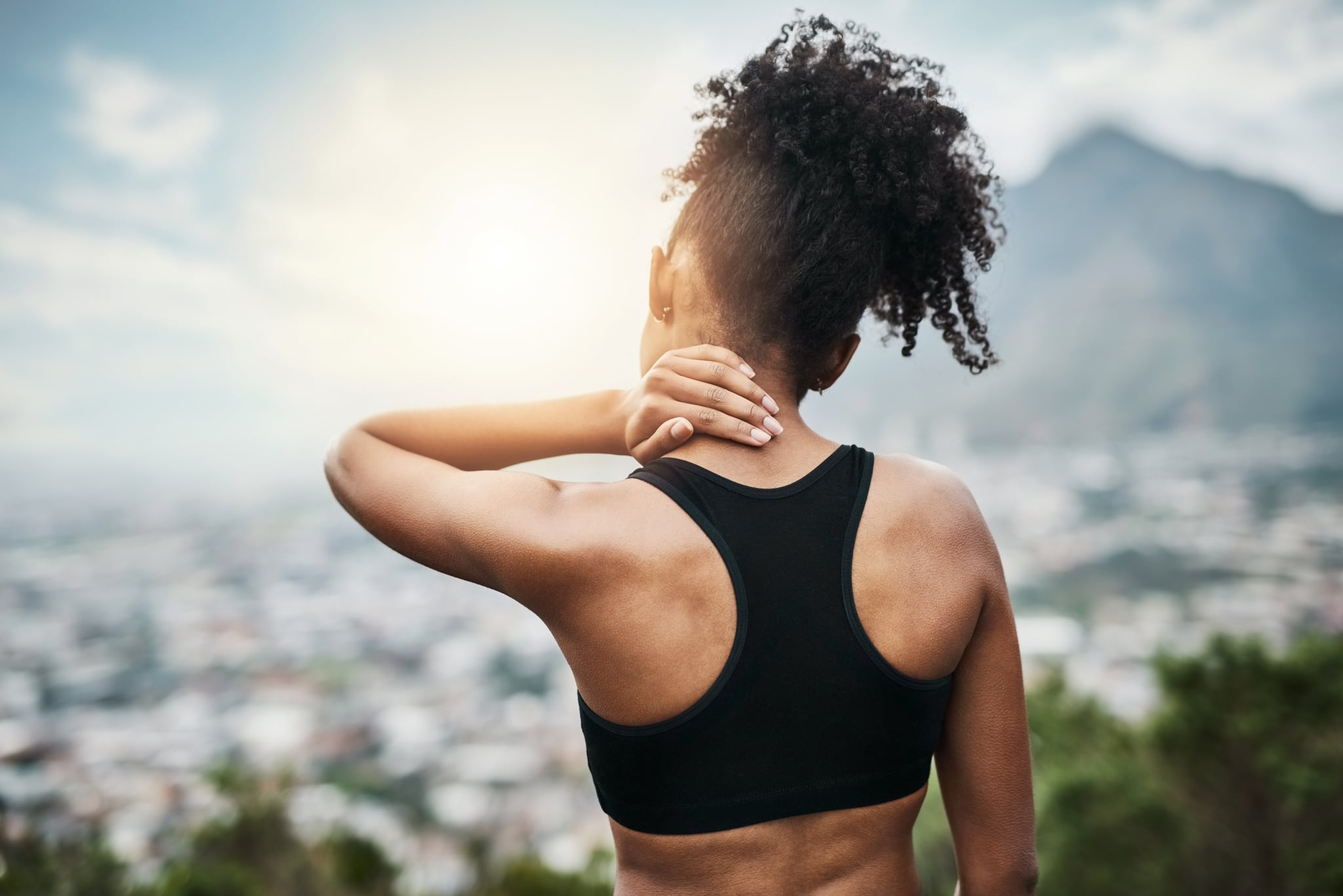 Rearview shot of a sporty young woman holding her neck while exercising outdoors