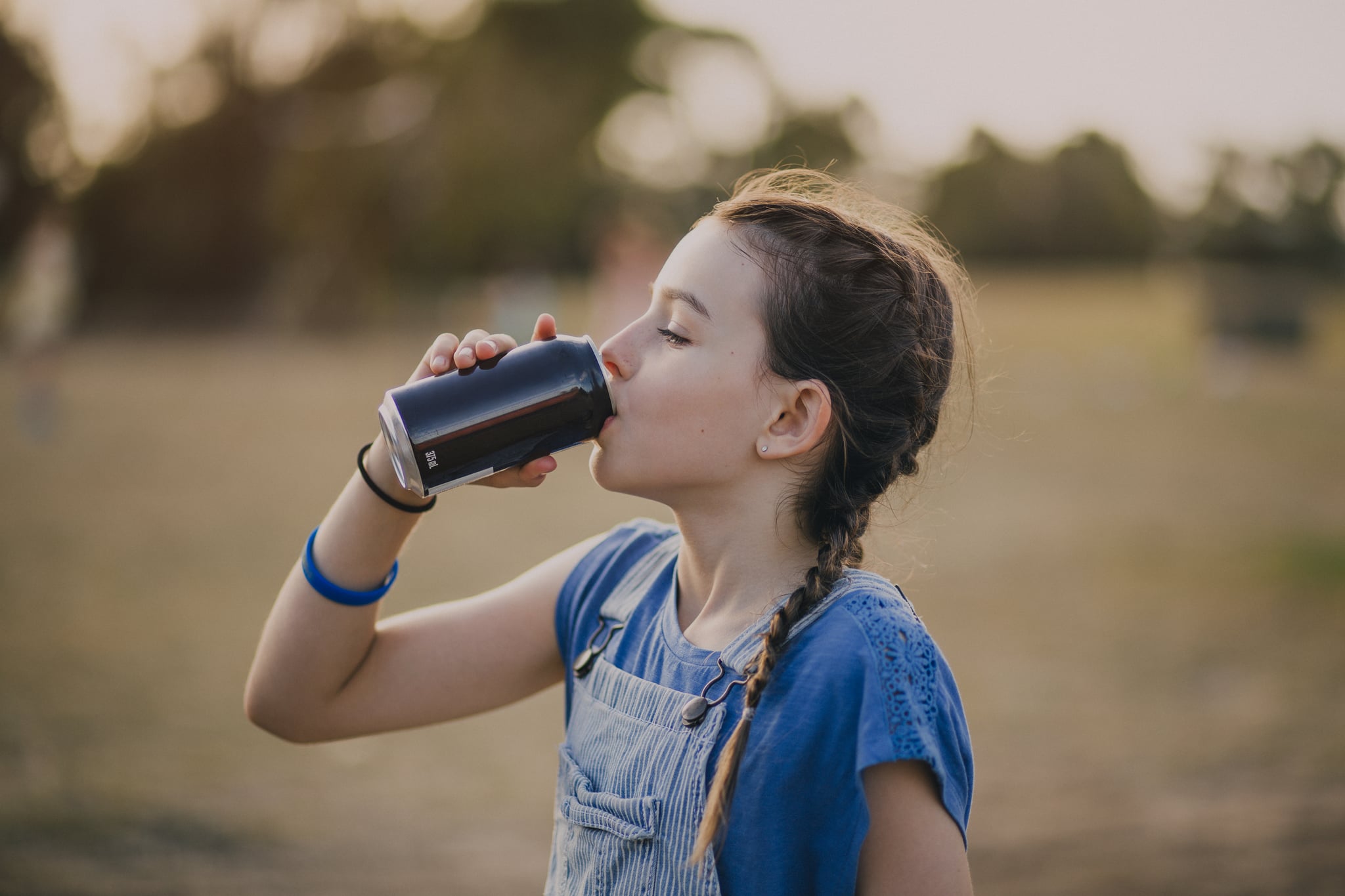 Little girl drinking from a soda can in a public park.