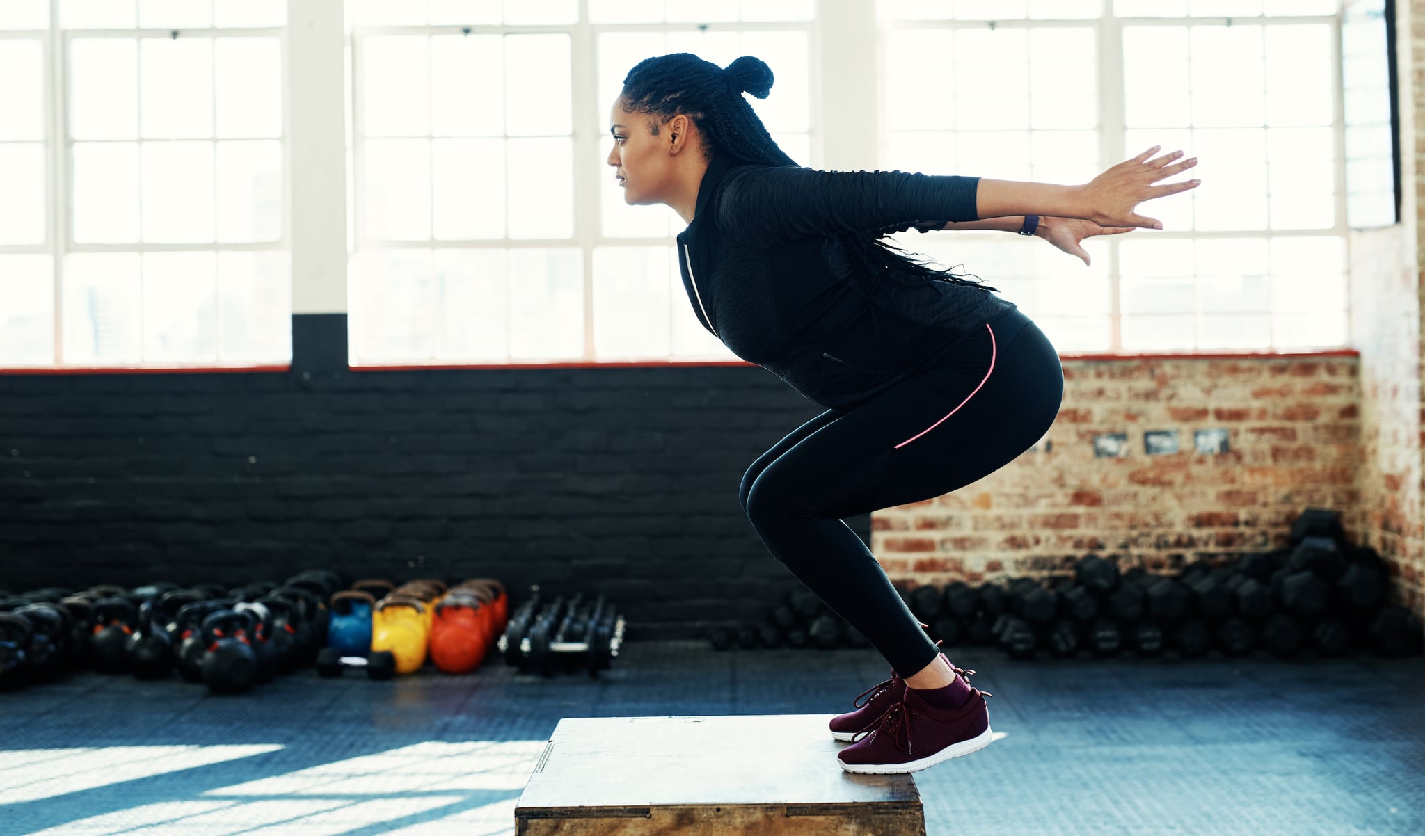 Shot of a young woman doing a exercise jump on a wooden block in a gym