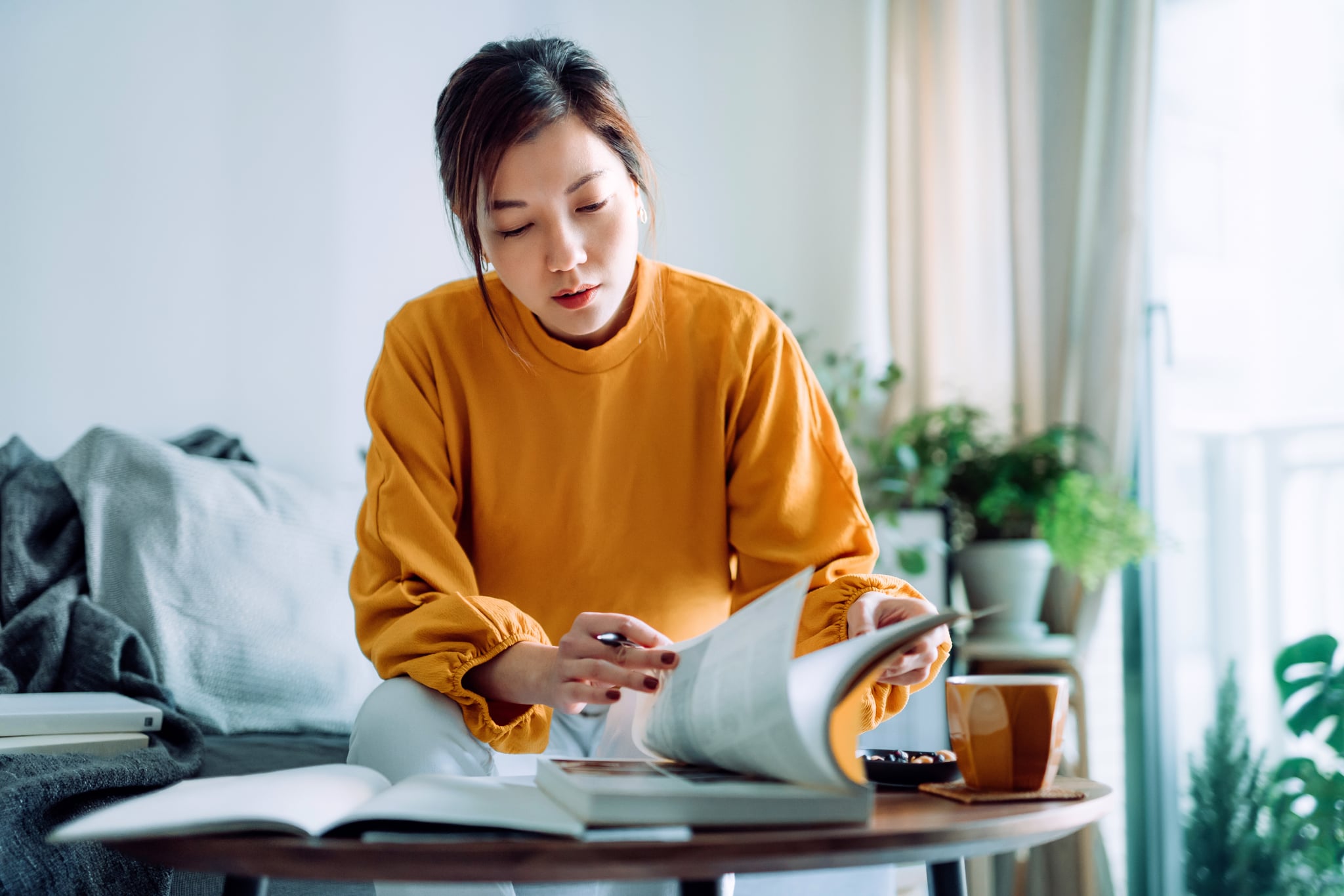 专注的年轻亚洲女性在家里看书和做笔记，专注于她的学习。继续教育理念