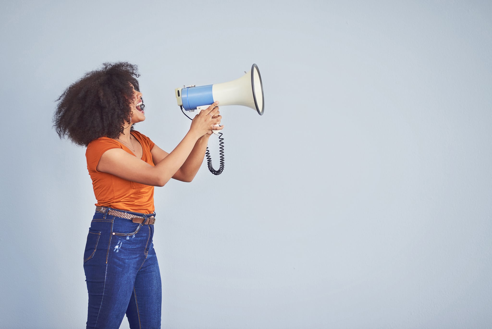 Studio shot of a young woman using a megaphone against a grey background