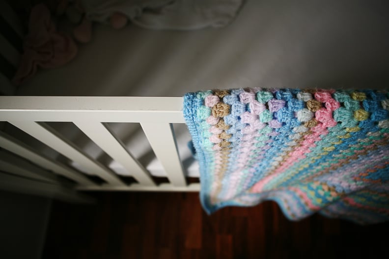 Empty baby's cot with shadows and crocheted blanket.
