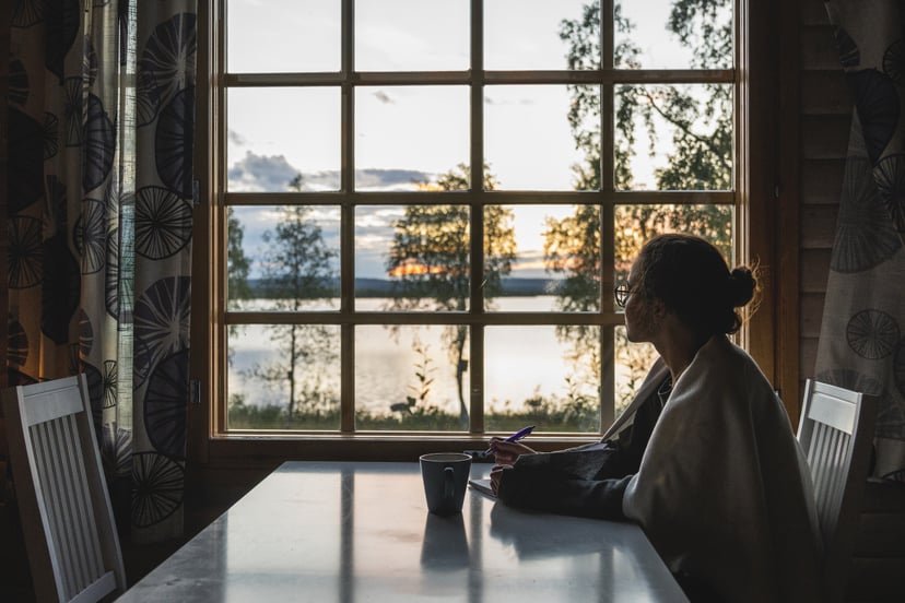 Finland, Lapland, young woman sitting at the window looking at a lake