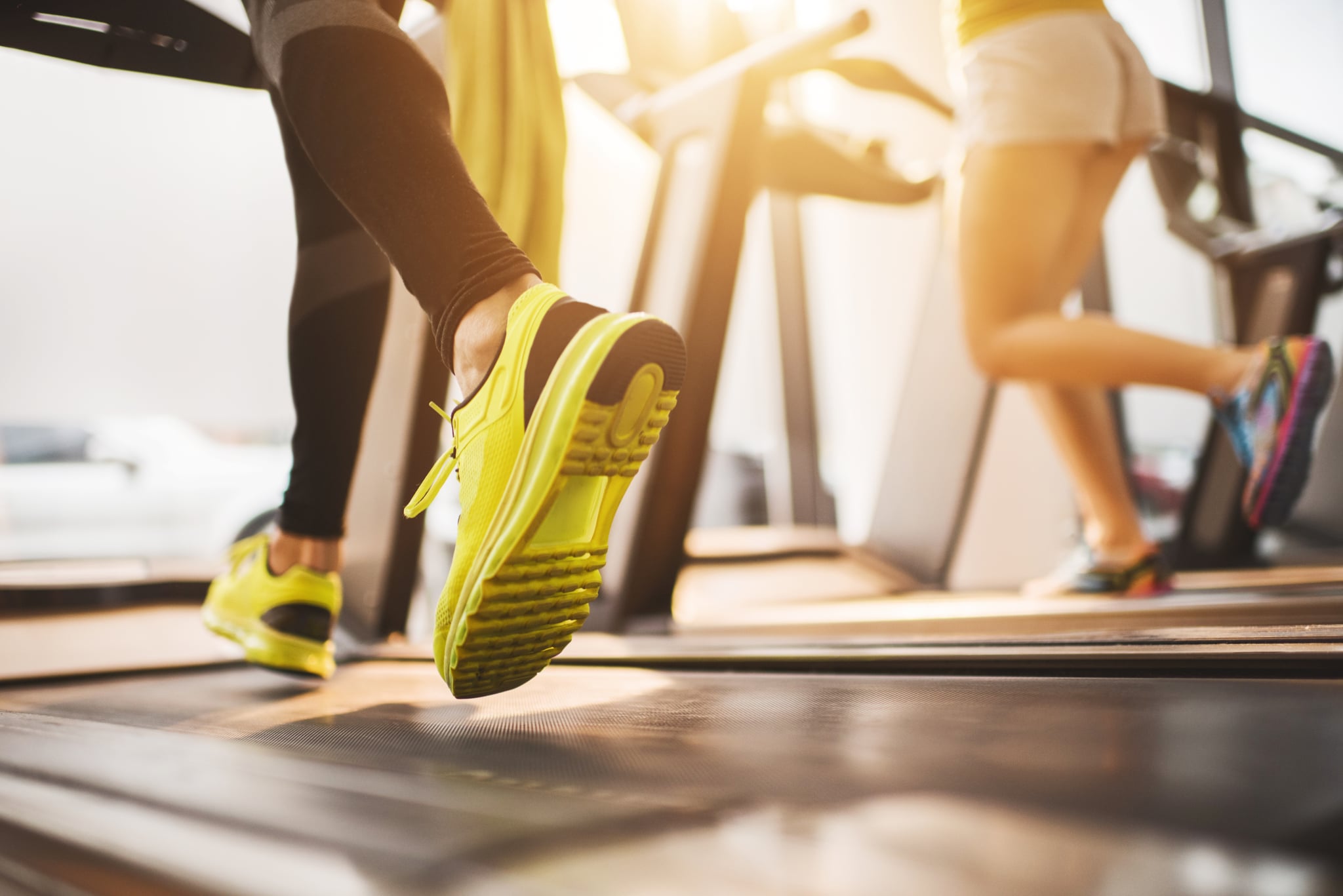 Two unrecognizable people exercising on treadmill in a health club.