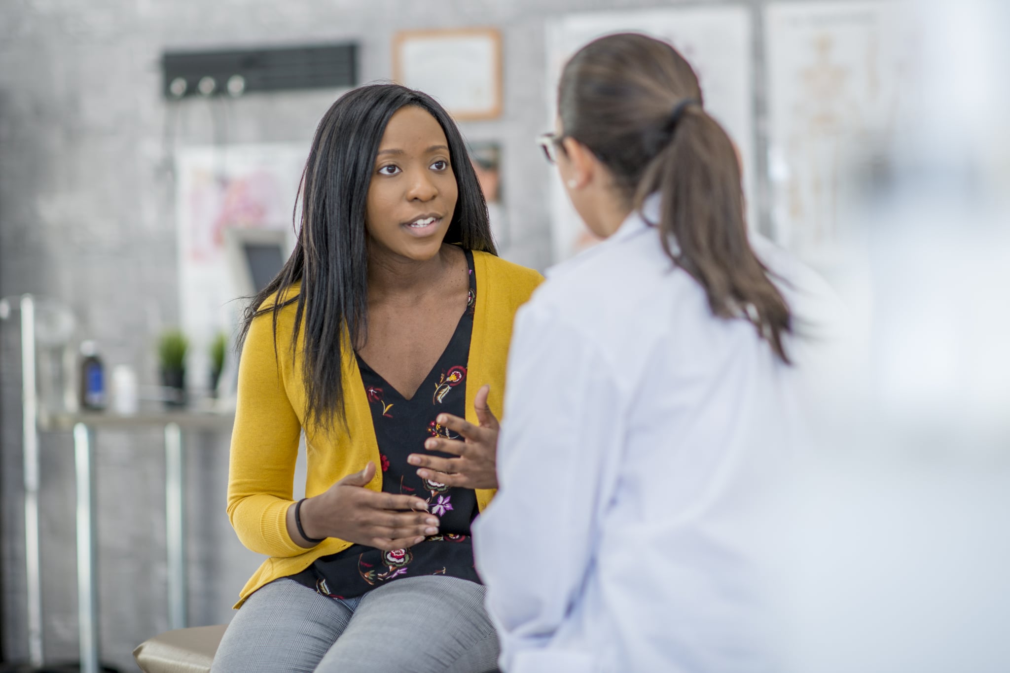 一名非洲裔妇女和她的医生在室内的一个诊所里。这位女士正坐着向医生描述她的症状。