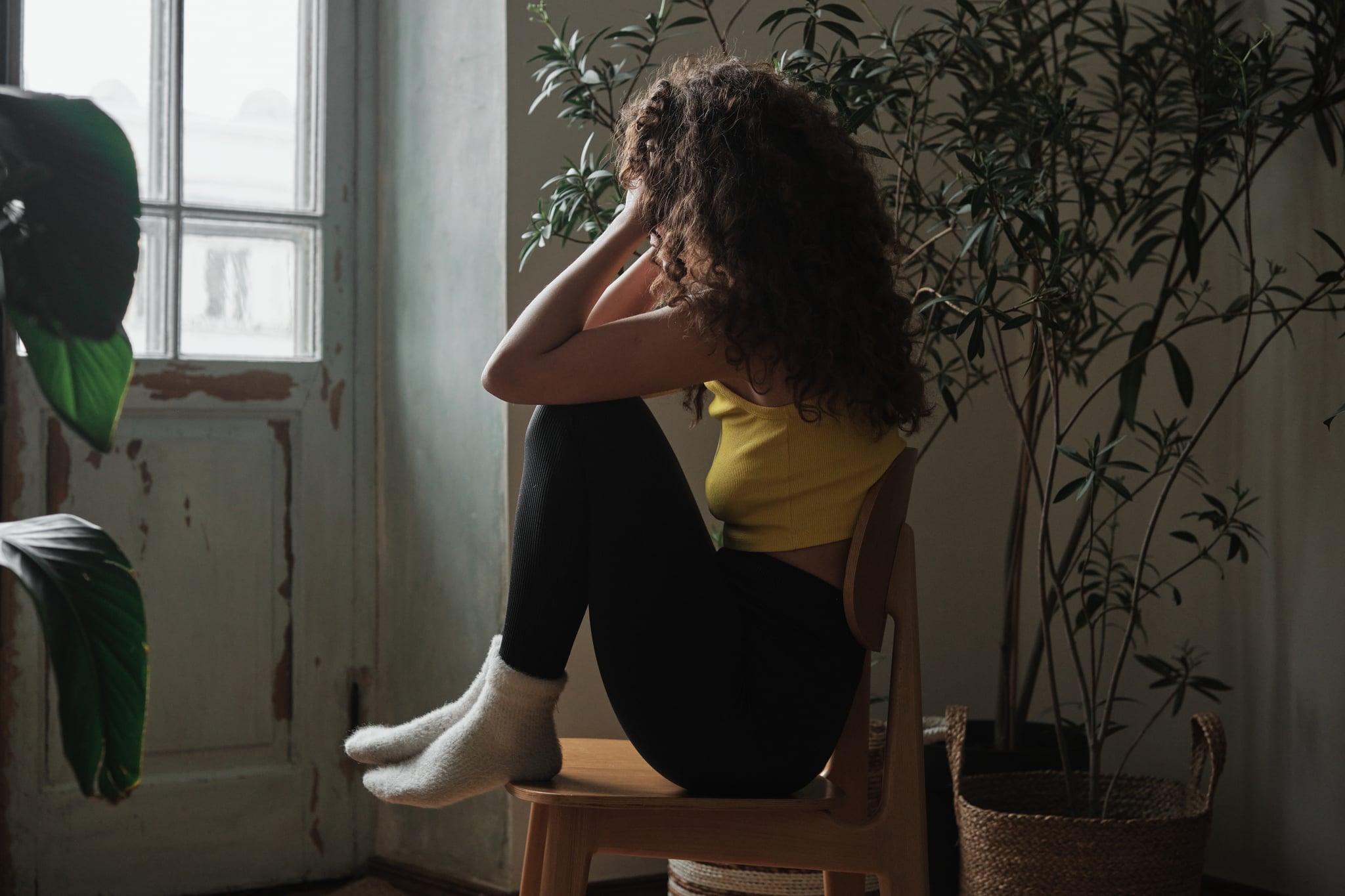 Lonely woman sitting on chair looking through window feeling sad and depressed.