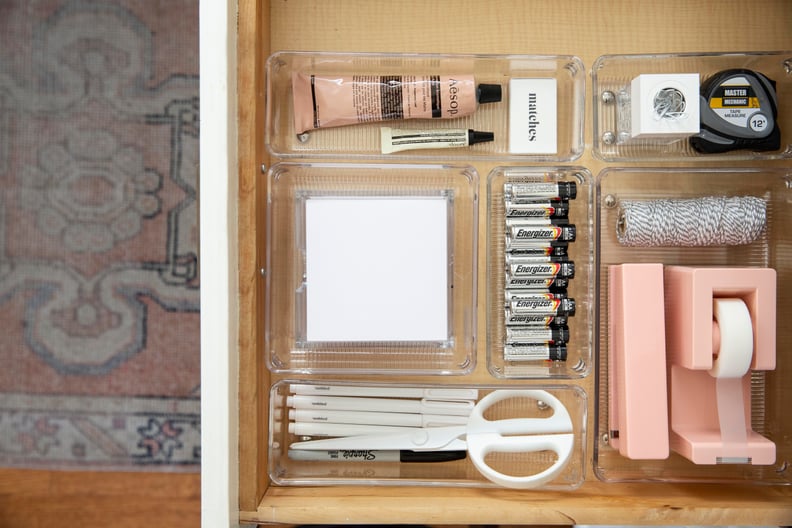 an organized desk drawer with tape, batteries, a stapler, and notepad