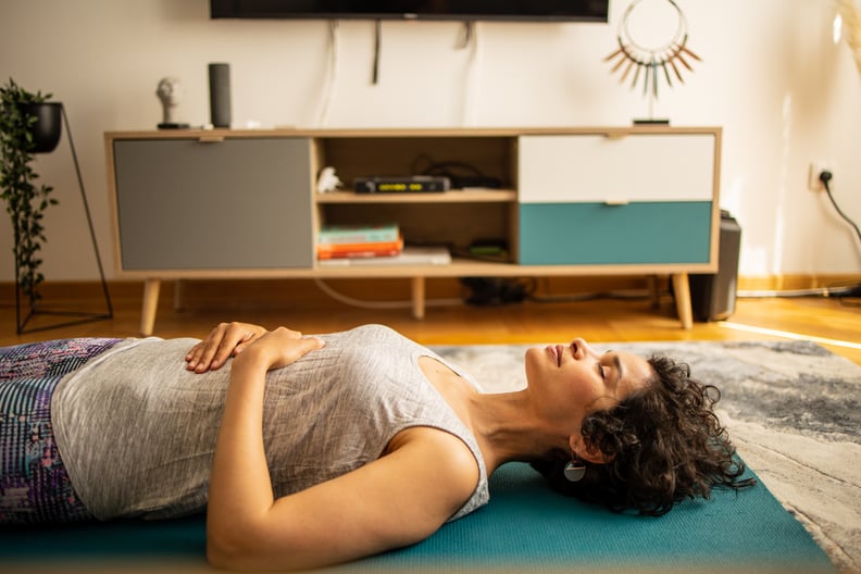 Side view of a Latin woman meditating on yoga mat at the living room. She is meditates with a video tutorial guide