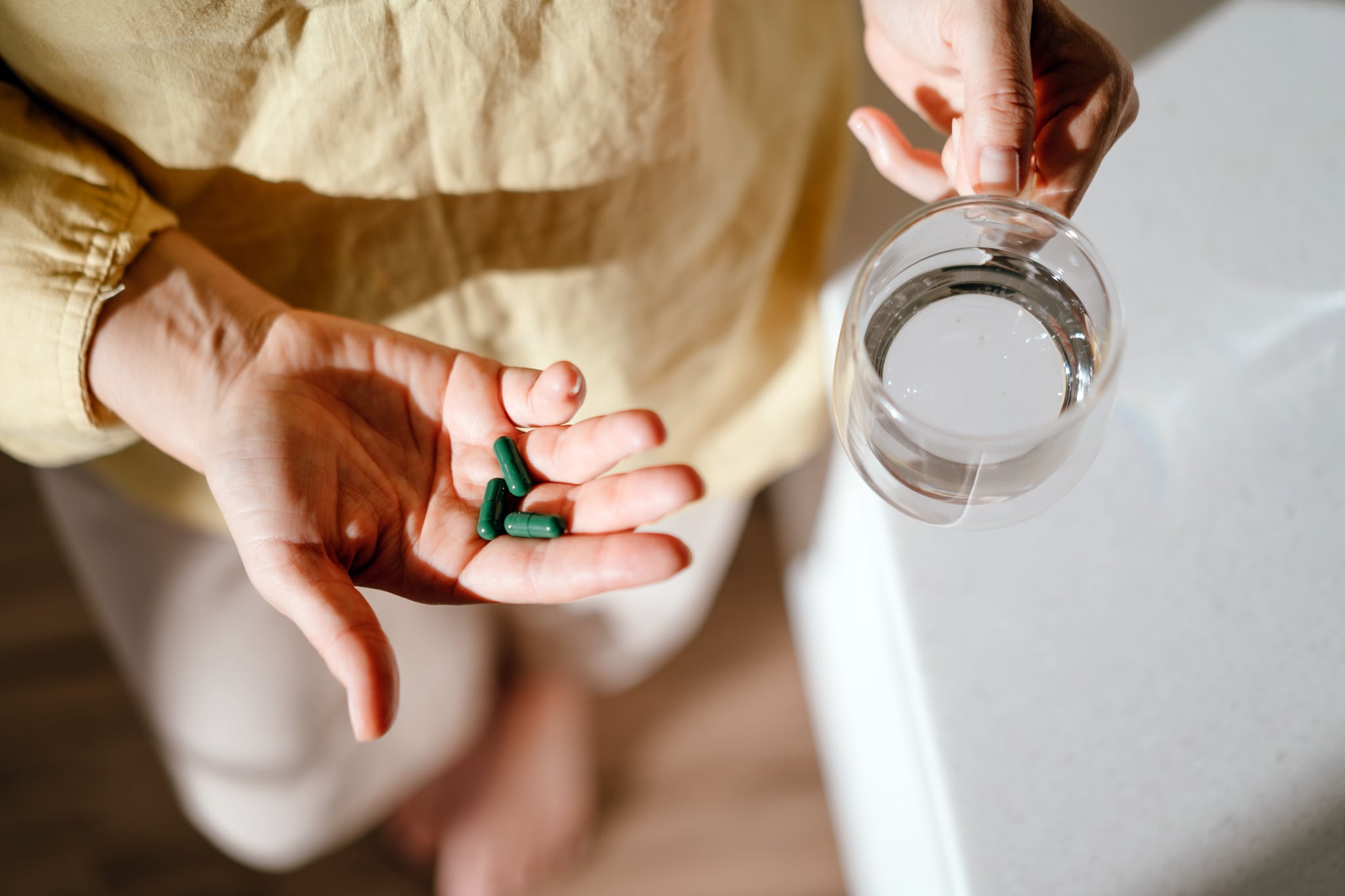 A woman standing at a table with green pills in her hand, sea moss supplements. A woman standing at a table with green pills in her hand, sea moss supplements.