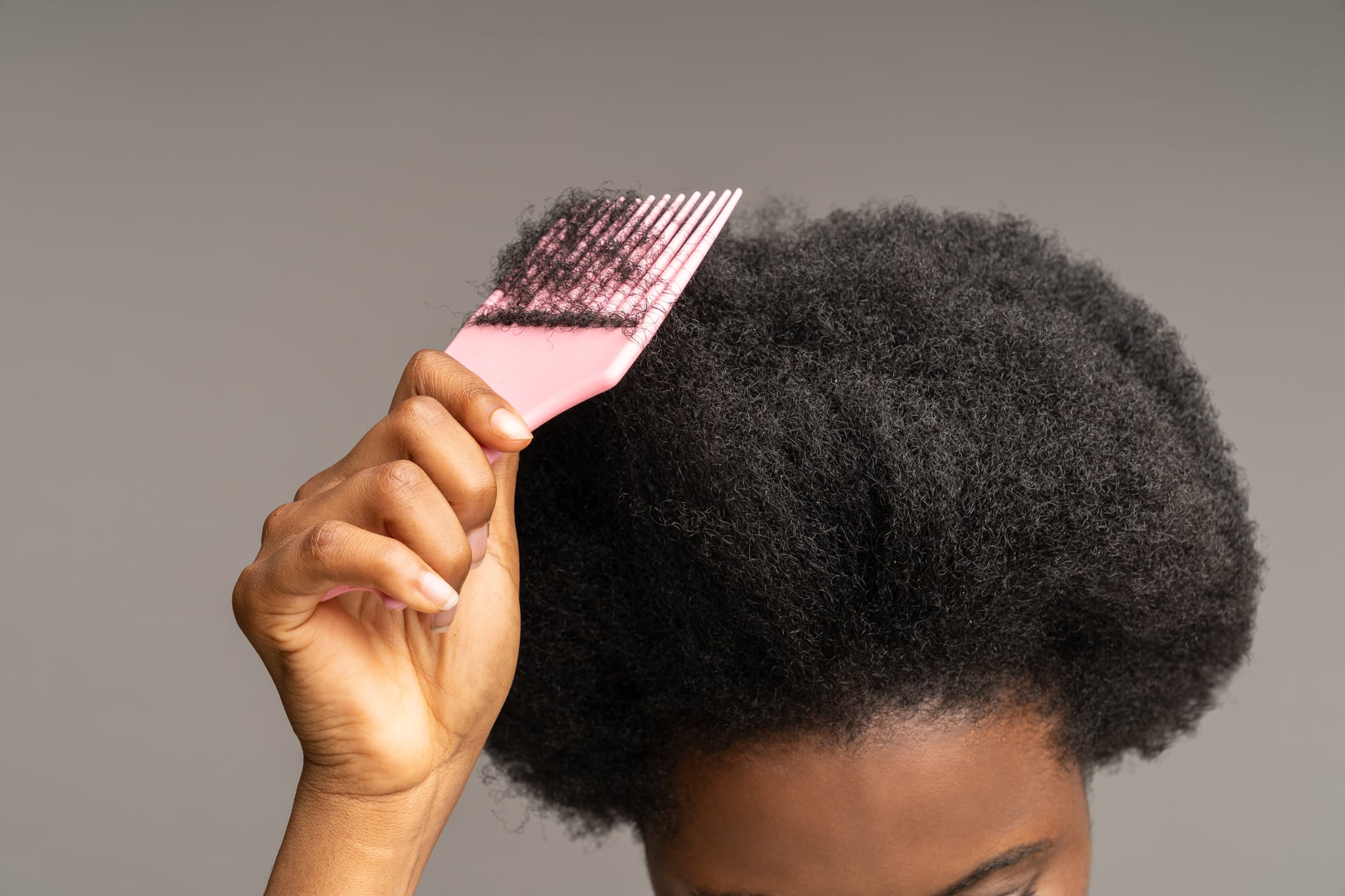 African woman combing curly hair. Cropped image of ethnic female hand holding hairbrush at head with wavy afro hairdo. Haircare equipment for ethnic hairstyle. Care and beauty for mixed race concept