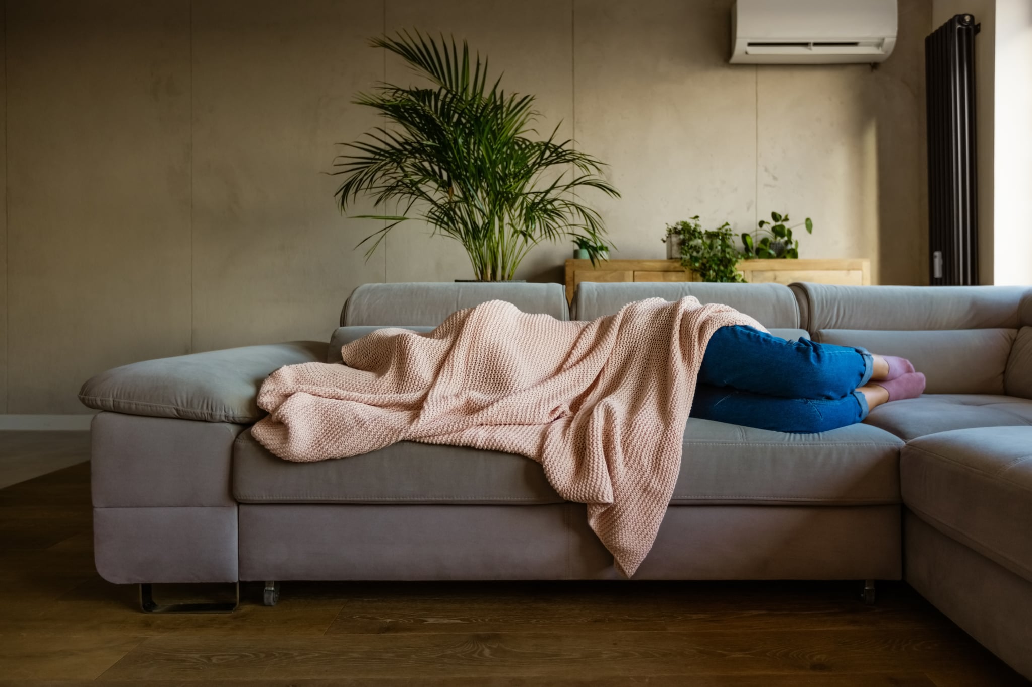 Young woman lying down on sofa in living room covered by blanket. Unrecognizable person.
