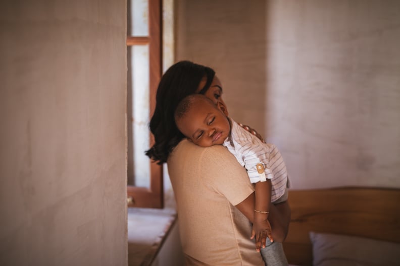 Young mother affectionately embracing and holding little sleeping son in her arms