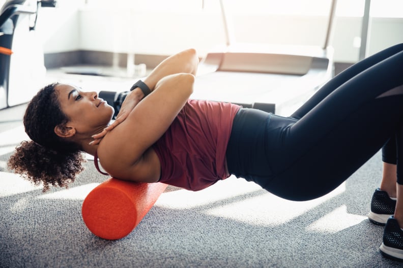 young woman stretching her back at the gym, using a foam roller