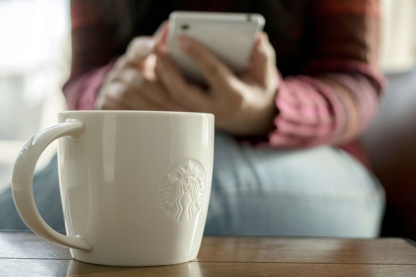 TIANJIN, CHINA - 2016/11/08: A Starbucks coffee cup on table, beside which a customer is reading on mobile phone.  At the end of November, a Chinese customer posted an open letter online to the chief executive of Starbucks in China to complain about the w