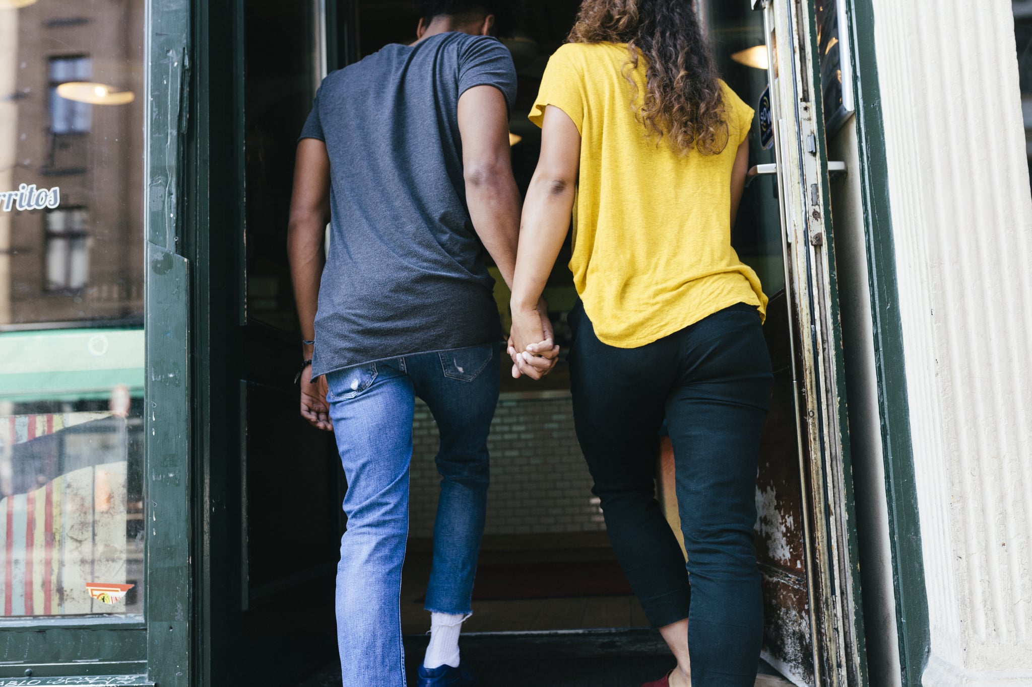 A couple holding hands and entering a restaurant together.