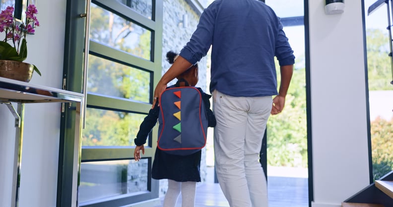 A Black father helps his daughter out the door as she goes to school.