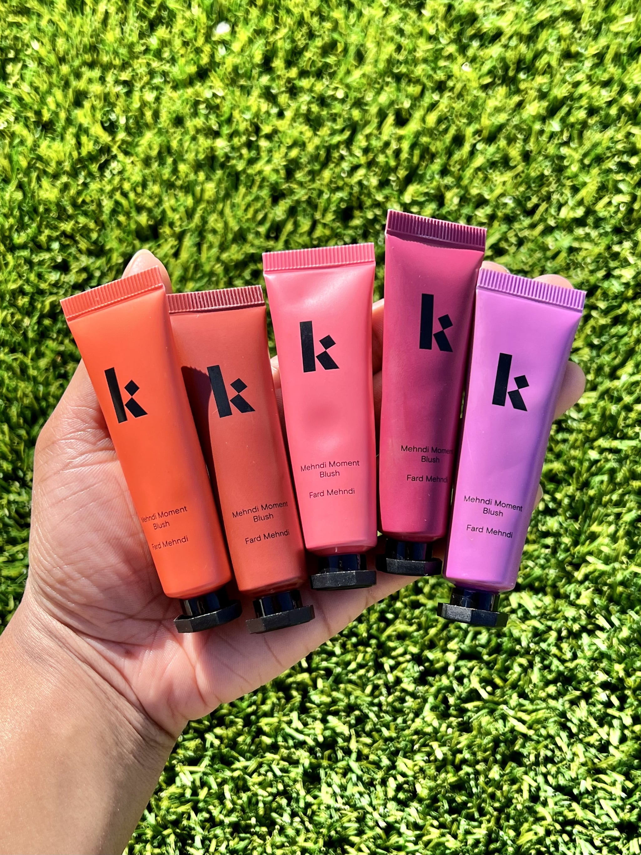 Woman holding the Kulfi Beauty Mehndi Moment Cream Blushes. From left to right: Garland Glow, Sandalwood Swirls, Pinky Promise, Blessed Berry, and Lucky Lotus.