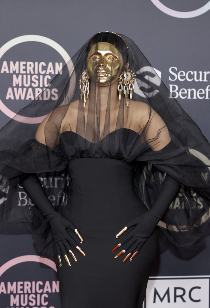 Cardi B made quite the entrance at the American Music Awards on Nov. 21. Once we got past the gold mask, gorgeous black gown, and matching veil, we were fixated on her mani game. The rapper, who's hosting Sunday night's show, wore her shiny gold nails — which complemented her dramatic mask — over her long black gloves attached to the sleeves of her dress. 
Similar to Beyoncé's nail gloves at the Grammys earlier this year, it looks like Cardi's nails were built right into the gloves using a trend inspired by drag queens. The cool metallic manicure featured a studded design and little piercings on the thumbs and pinkies. And upon taking a closer look at Cardi's ears, you'll even see manicured fingers dangling from her earrings. Have a peek at the host's fun nail look ahead.

    Related:

            
            
                                    
                            

            Olivia Rodrigo Tried Many Different Nail Art Designs Before Landing on This Manicure For the AMAs
