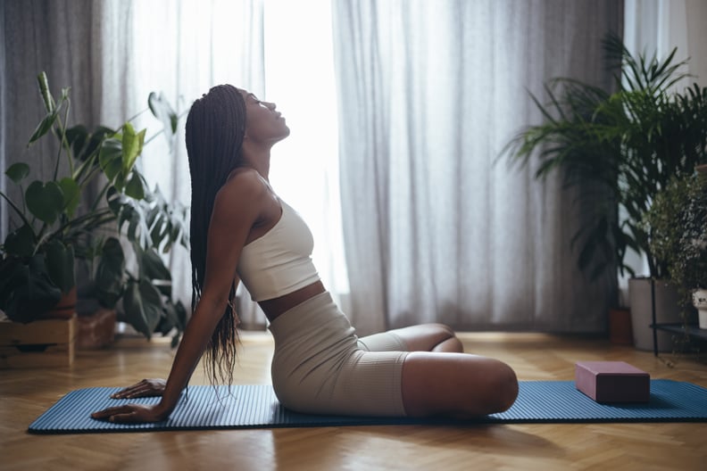 Side view of young woman sitting on blue yoga mat ready for a somatic training session
