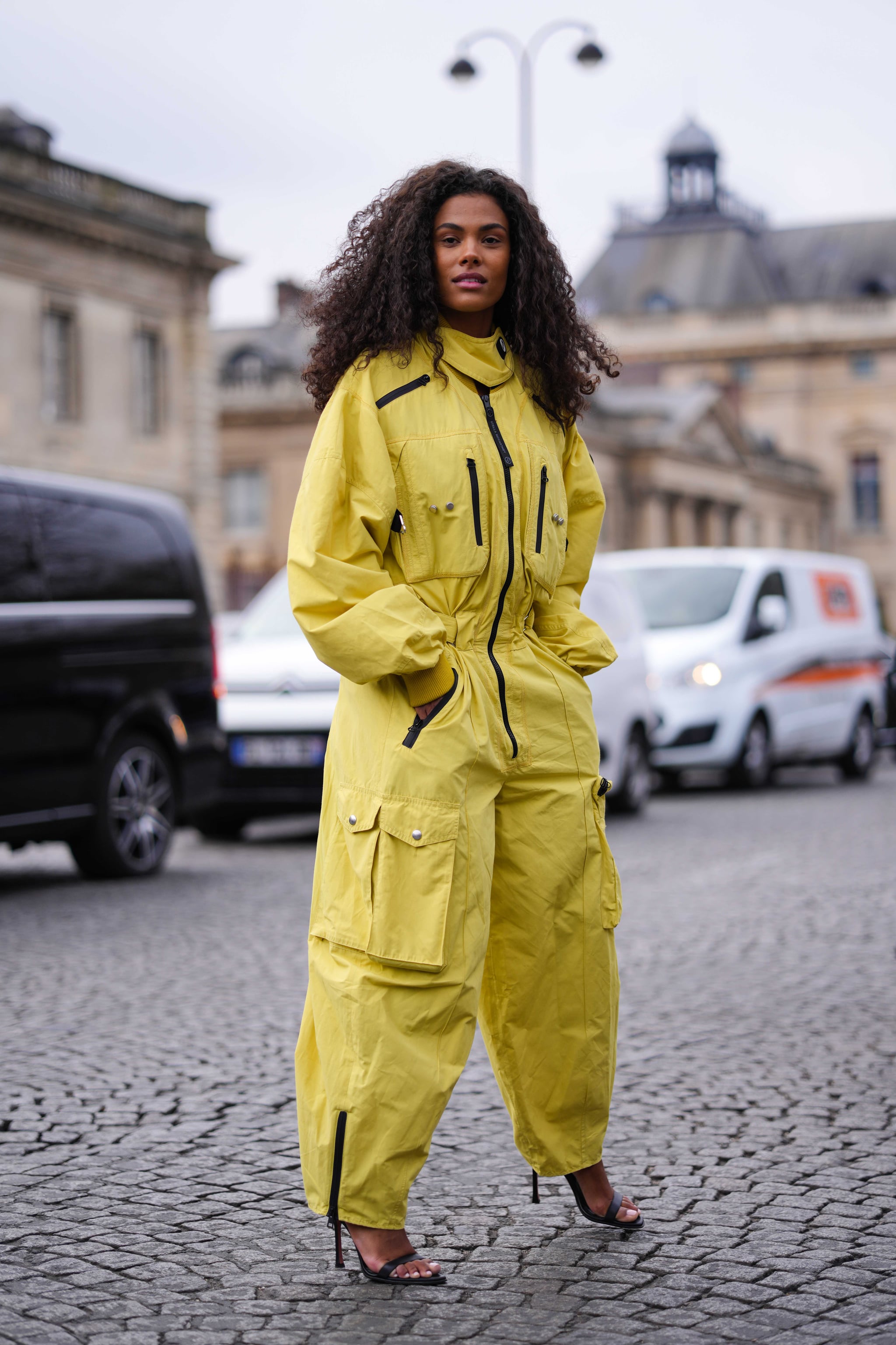 PARIS, FRANCE - MARCH 06: A guest wears a yellow high neck / puffy long sleeves / black zipper details cargo jumpsuit, black shiny leather heels strappy sandals , outside Stella McCartney, during Paris Fashion Week - Womenswear Fall Winter 2023 2024, on March 06, 2023 in Paris, France. (Photo by Edward Berthelot/Getty Images)