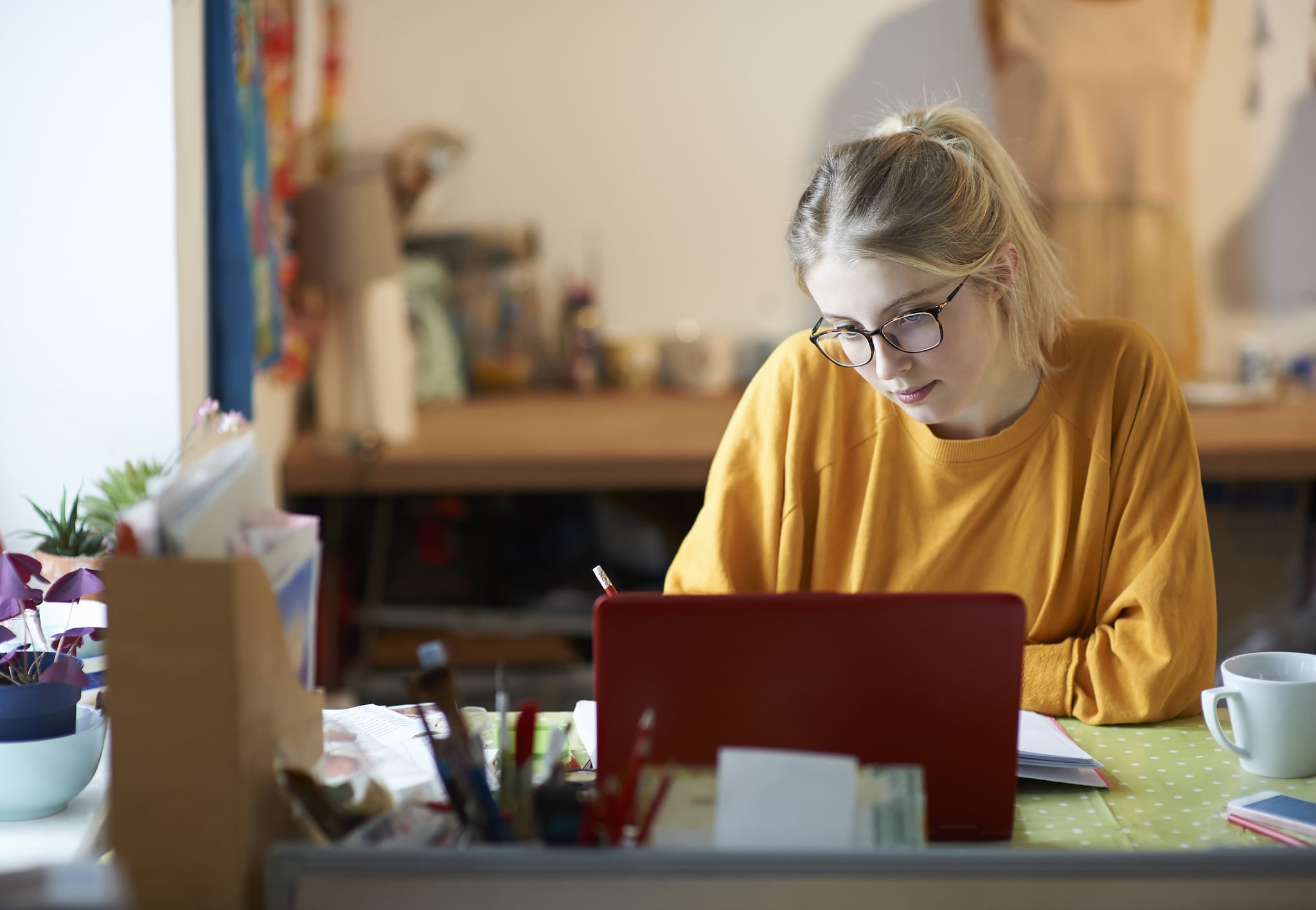 A young woman student at home with her laptop making notes and studying.