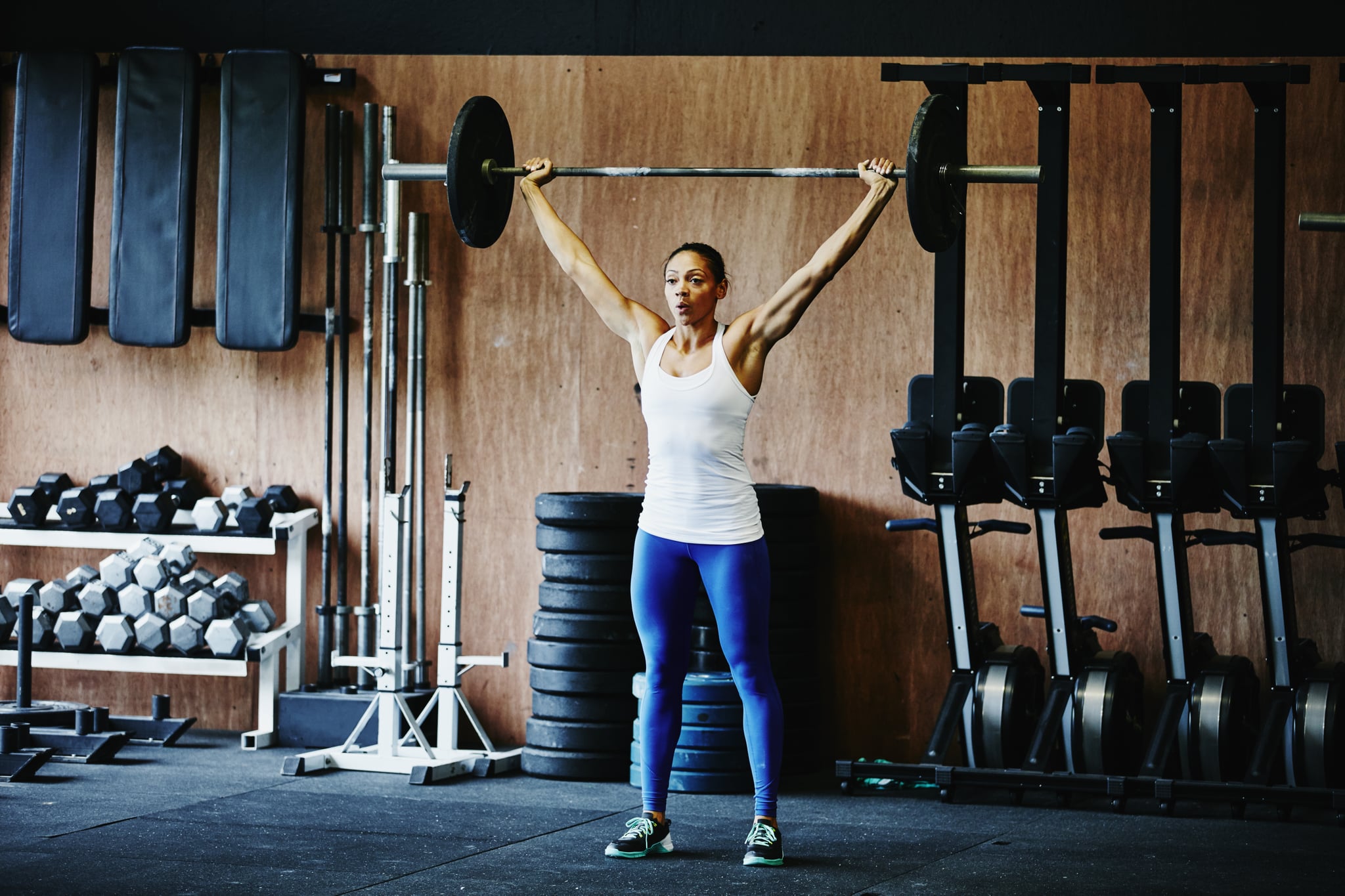 Woman pressing barbell overhead during crossfit training workout in gym