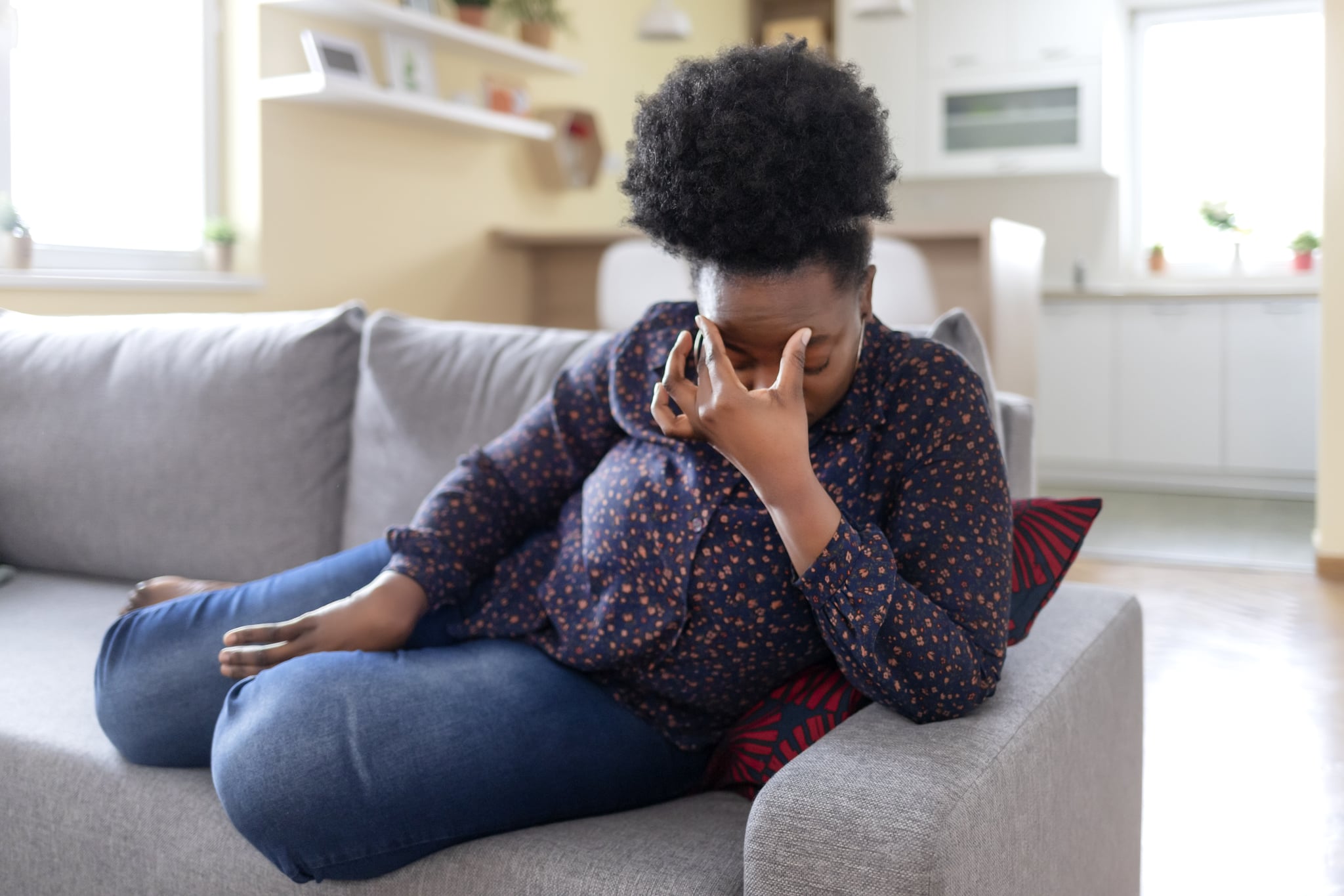 Young Black Woman Sitting on a Couch, Holding Her Head, Having a Strong Headache