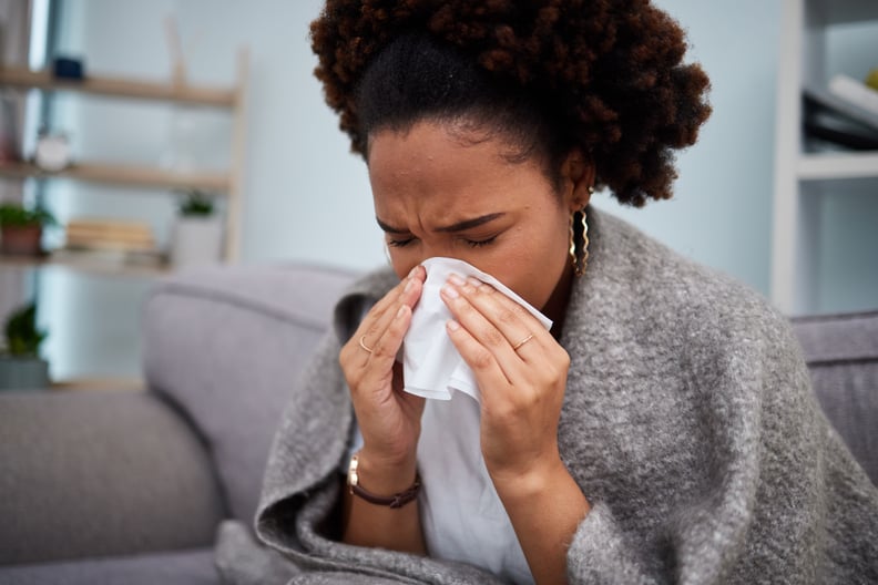 Woman sitting on the couch, blowing her nose — dealing with one of the different types of flu.