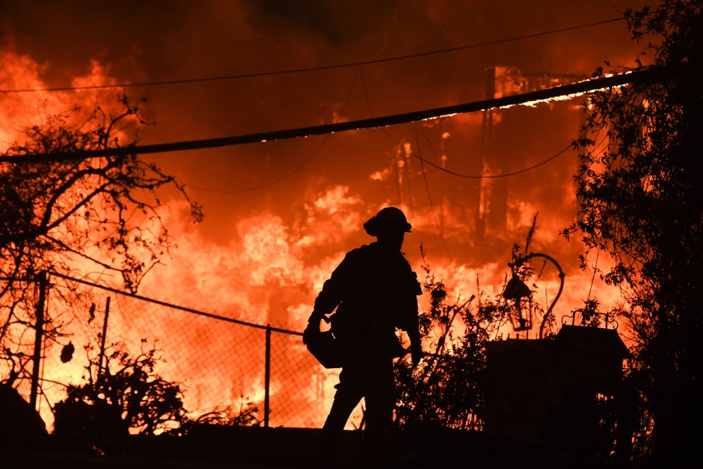 A home burns along the Pacific Coast Highway, with a firefighter on the scene.