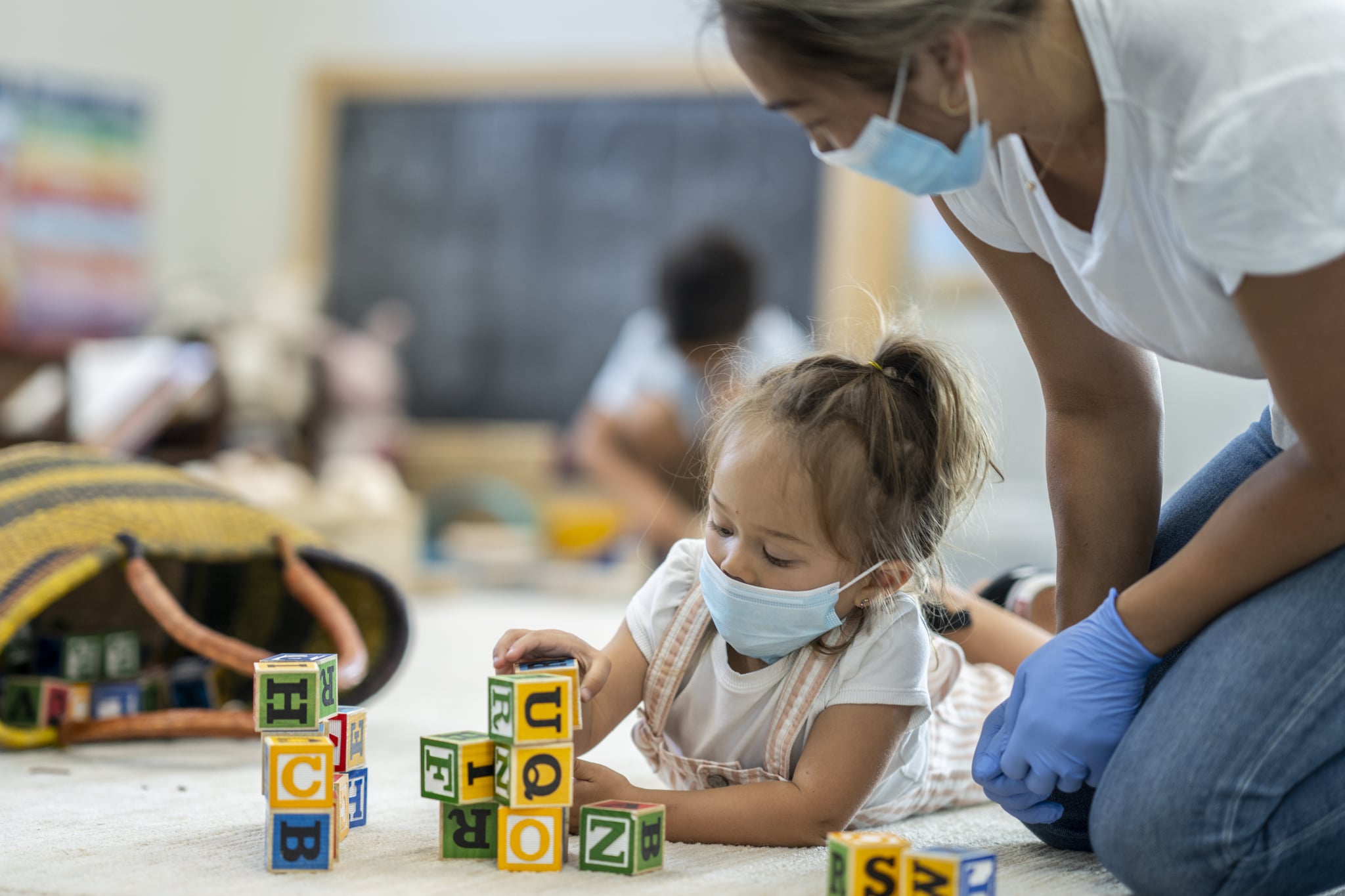 3 year old girl playing at daycare while wearing a protective face mask to protect from the transfer of germs during phase 2 of reopening during COVID-19.