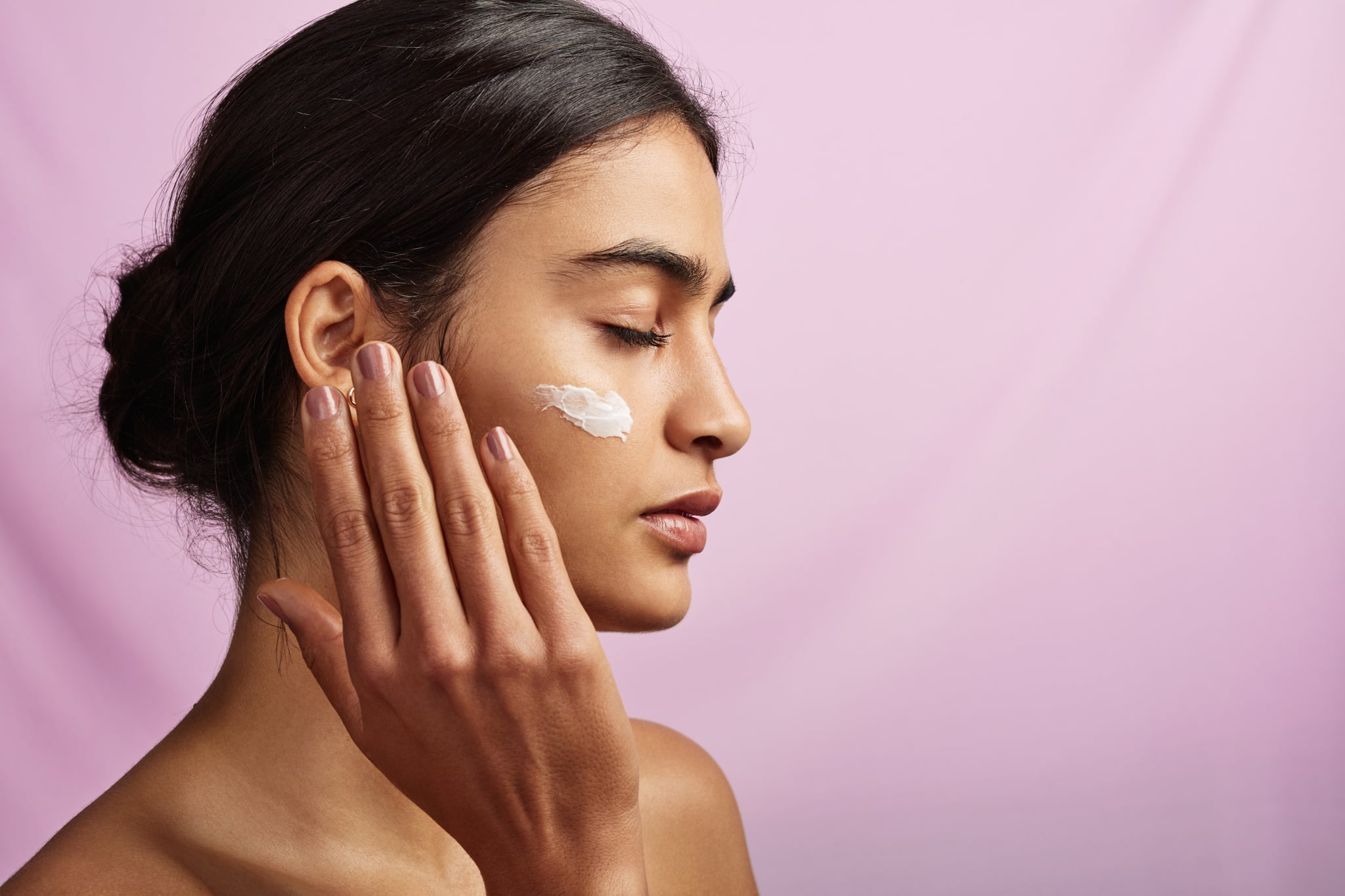 Studio shot of a beautiful young woman applying moisturiser to her face
