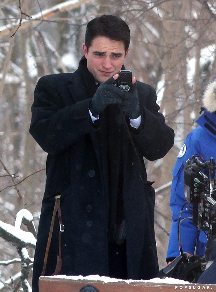 Robert Pattinson has been lying low for a while, but we finally got a glimpse at what he's been up to — and he looks completely different! Not only has Rob shaved his goatee, but he also dyed his hair black to play photographer Dennis Stock in the upcoming film Life. Shooting is currently under way in Toronto, and Robert braved the cold for a snowy scene on Tuesday, laughing and snapping photos of a bench. 
Back in September, we spoke to Rob's costar Dane DeHaan, who portrays James Dean in the film, and he admitted he was "terrified" but excited to work with a "great guy" like Rob. Dane is certainly already looking his part, showing off James's signature look in some new photos from set. Life isn't due out until at least next year, but this Summer, Robert will show off another transformation in The Rover, in which he stars as an injured robber forced to help Guy Pearce's character find his stolen car in the desert. For more pics of Rob filming, keep scrolling, then check out some more of him walking around set on Wednesday.