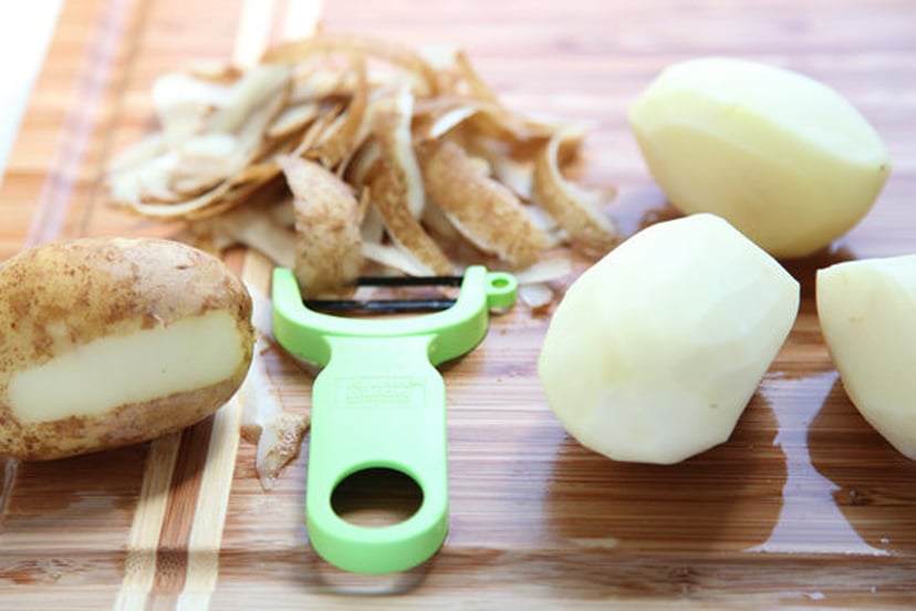Potatoes and peeler on wooden chopping board