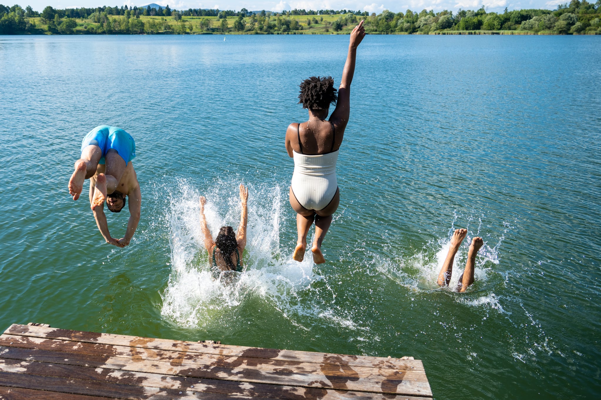 Four friends diving into lake during sunny day.