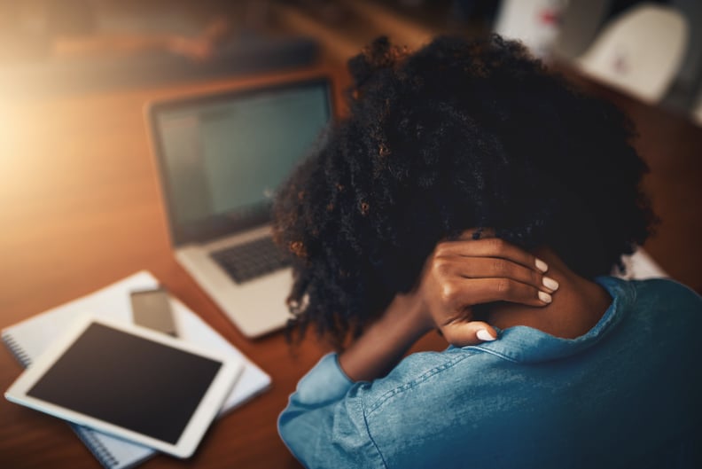 Rearview shot of a young woman holding her neck in pain while working at home