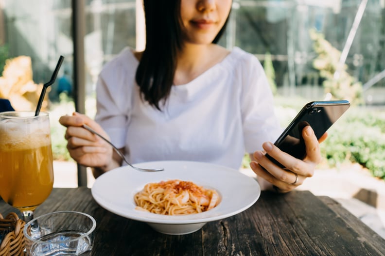 Smiling woman using her mobile phone while having meal at a cafe outdoors
