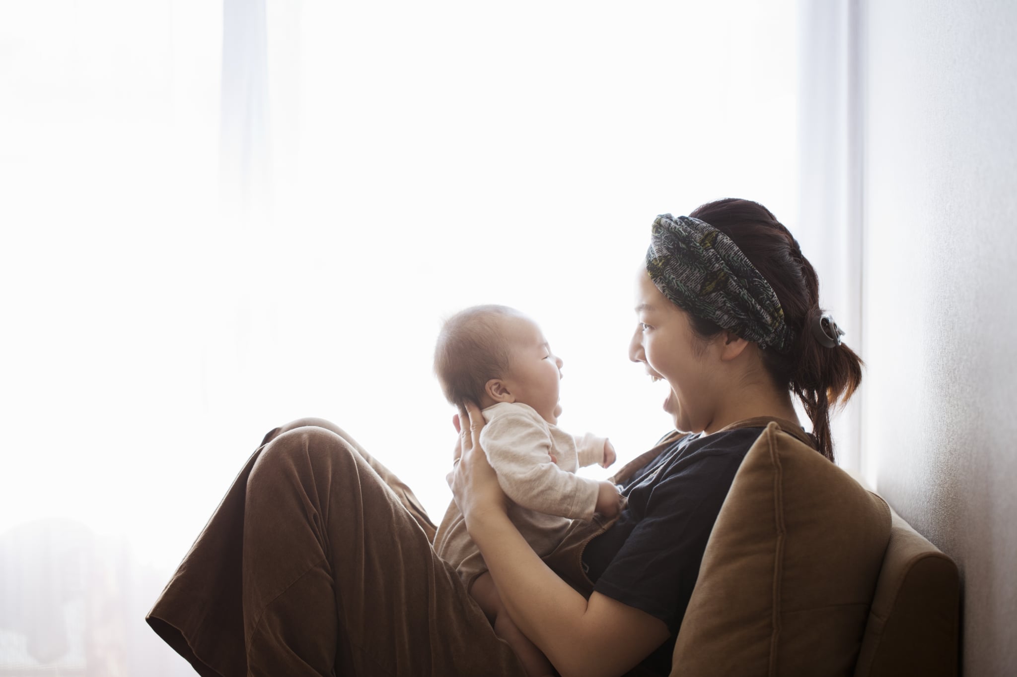 A mother carrying her baby on sofa, and they are looking each other with smiling.