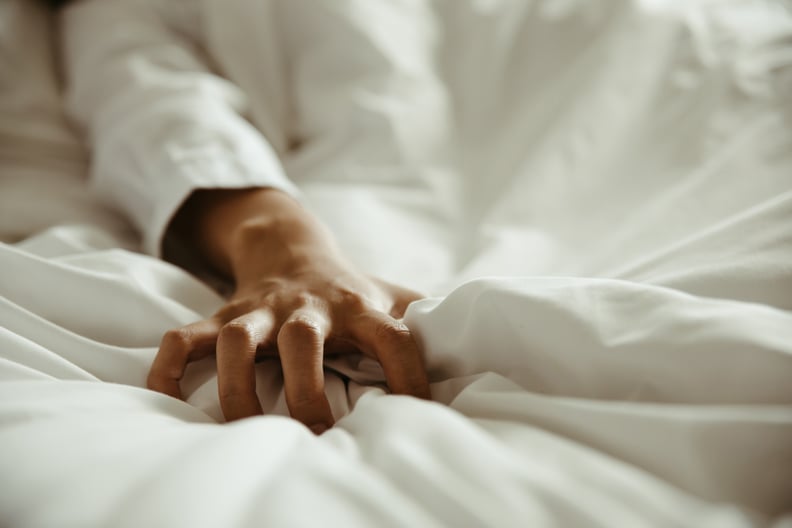 Close up of a woman's hand as she pulls on white sheets in ecstasy.