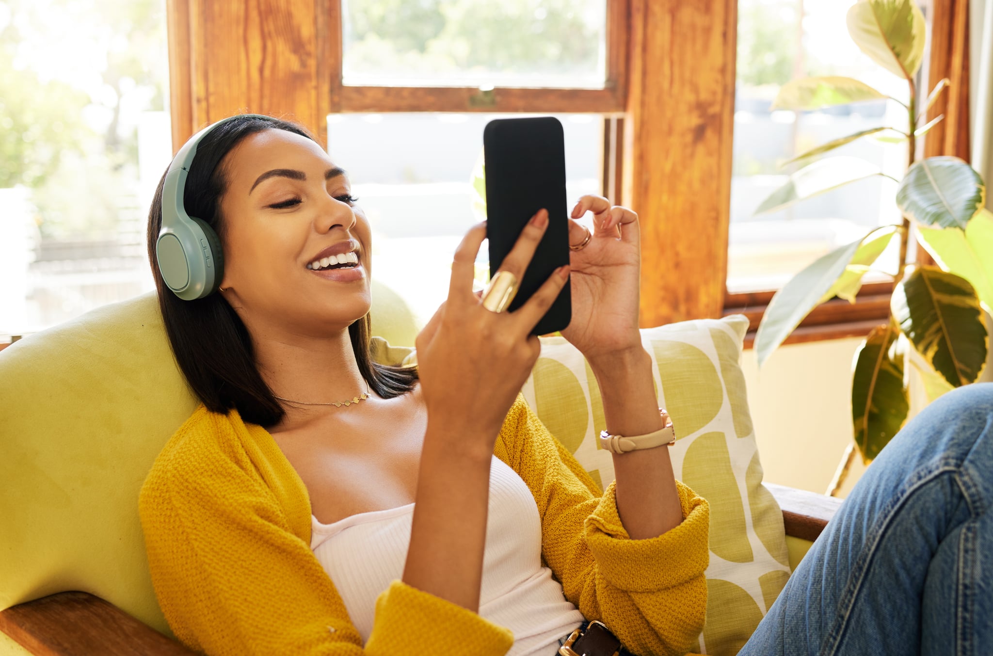 Woman updating contact names on her smartphone and listening to music on headphones while comfortable and relaxing in a bright living room.