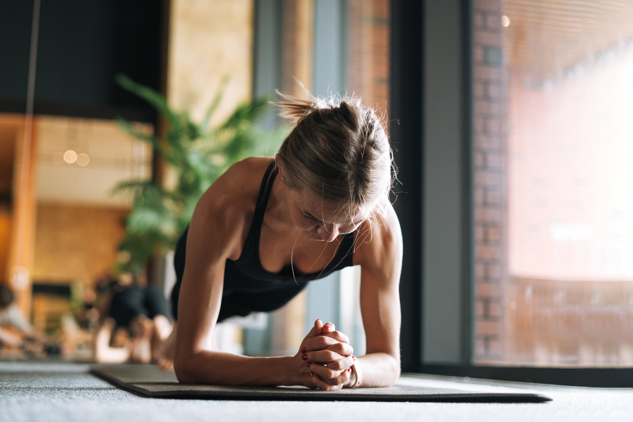 Young woman in sportswear doing plank exercise on mat in modern studio.