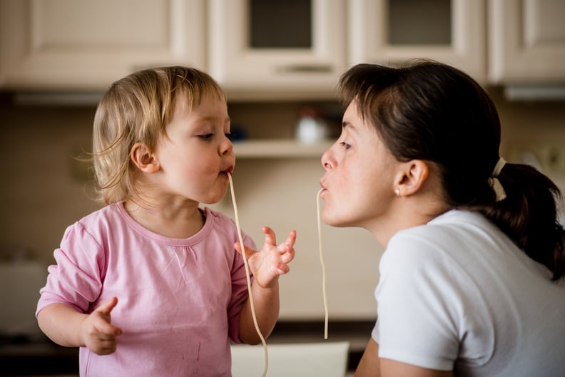 Mother and her little child sucking together spaghetti noodles.