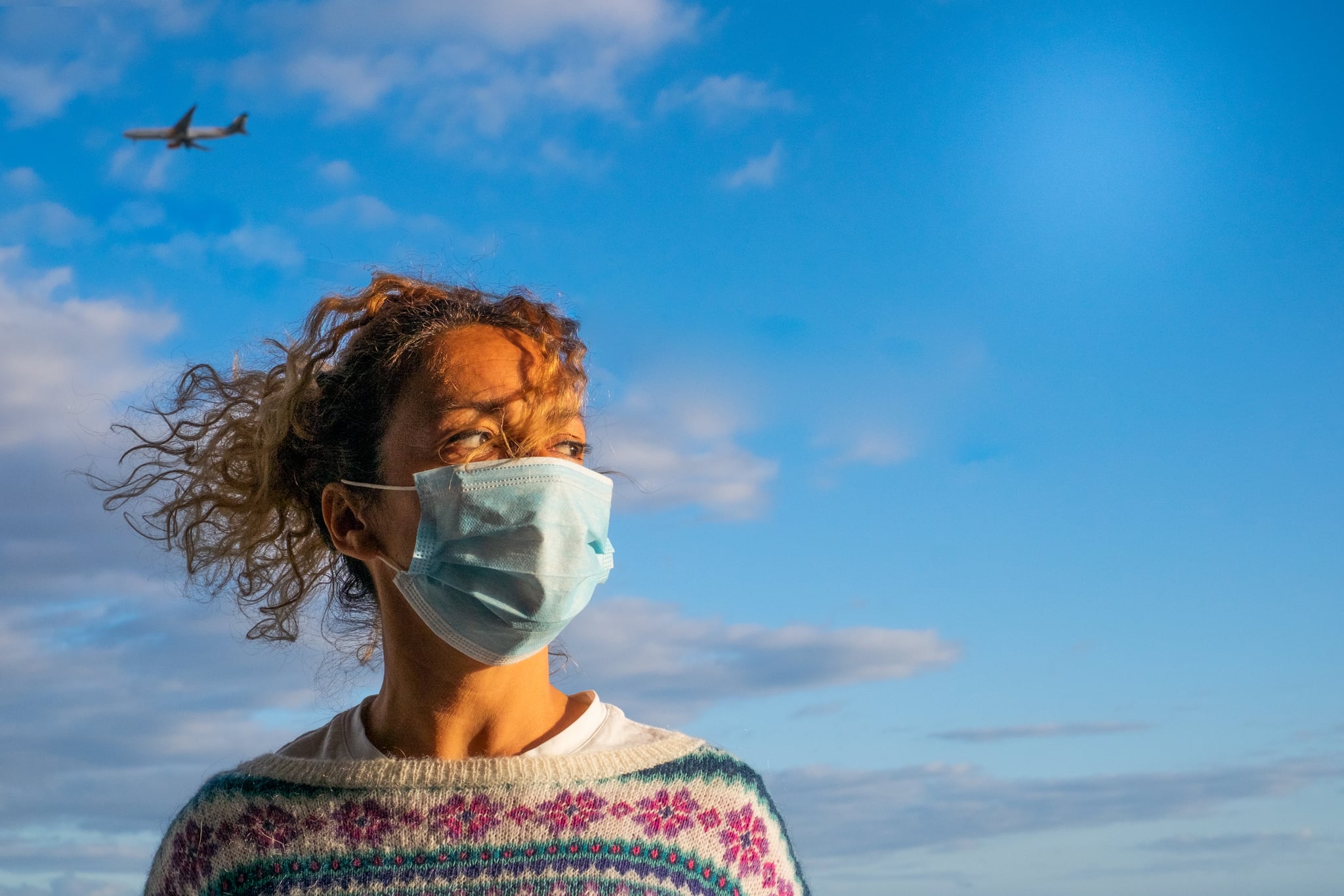 one curly and beautiful woman wearing medical mask to prevent any type of disease or virus like coronavirus or covid-19 - airplane inside of her head at the background like risky vacations hazard