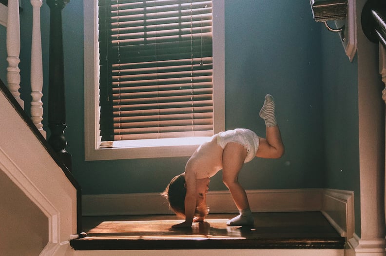 Two years old toddler wearing diapers doing Yoga on the stairs at home.