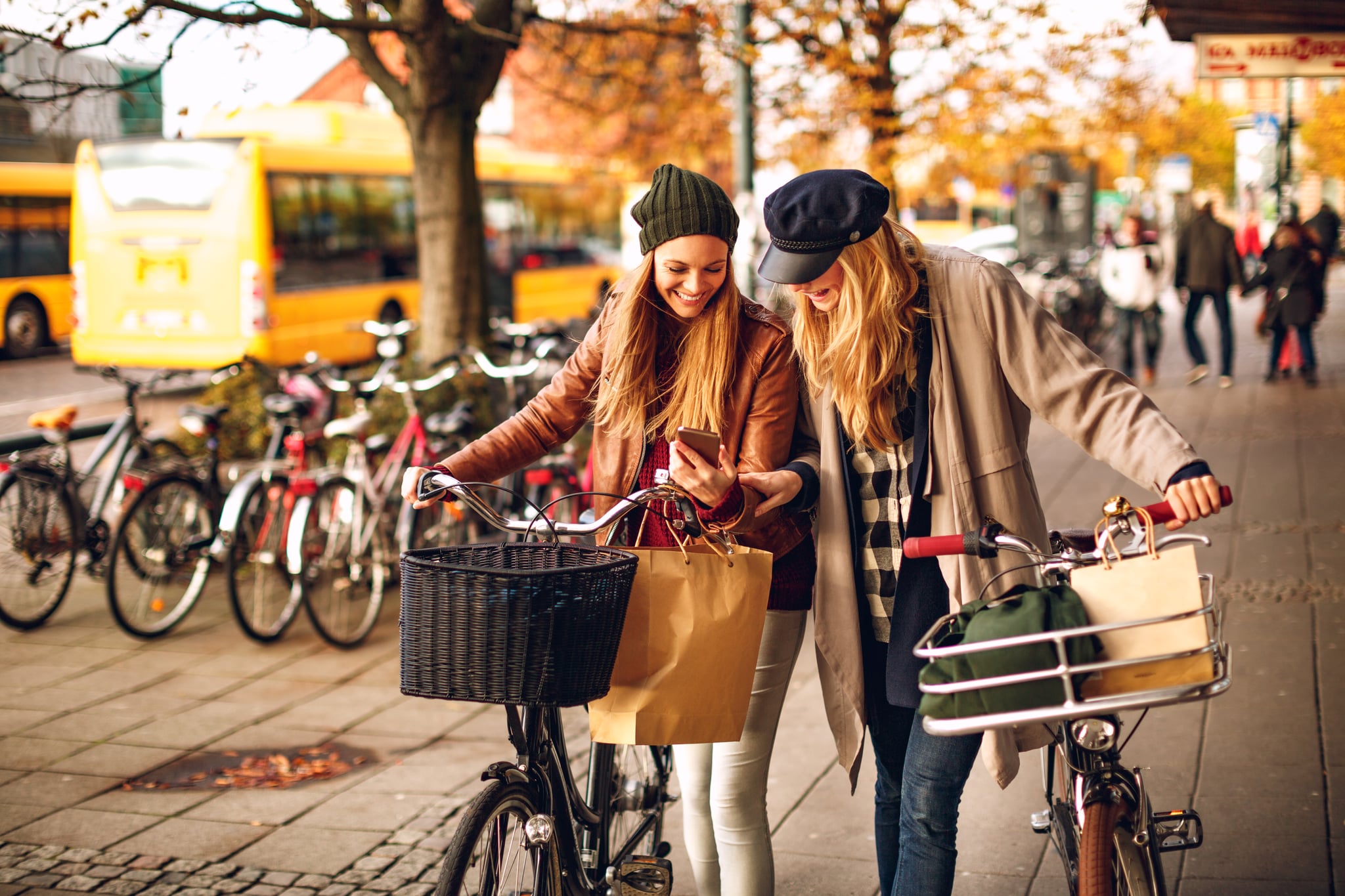 Close up of two friends leading their bicycles and using their phone