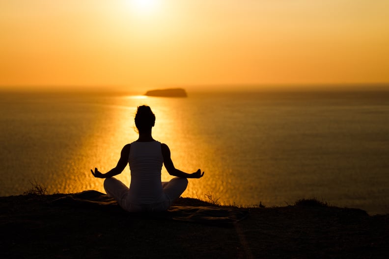 Silhouette of a relaxed woman meditating in Lotus position on a hill above the sea at sunset. Copy space.