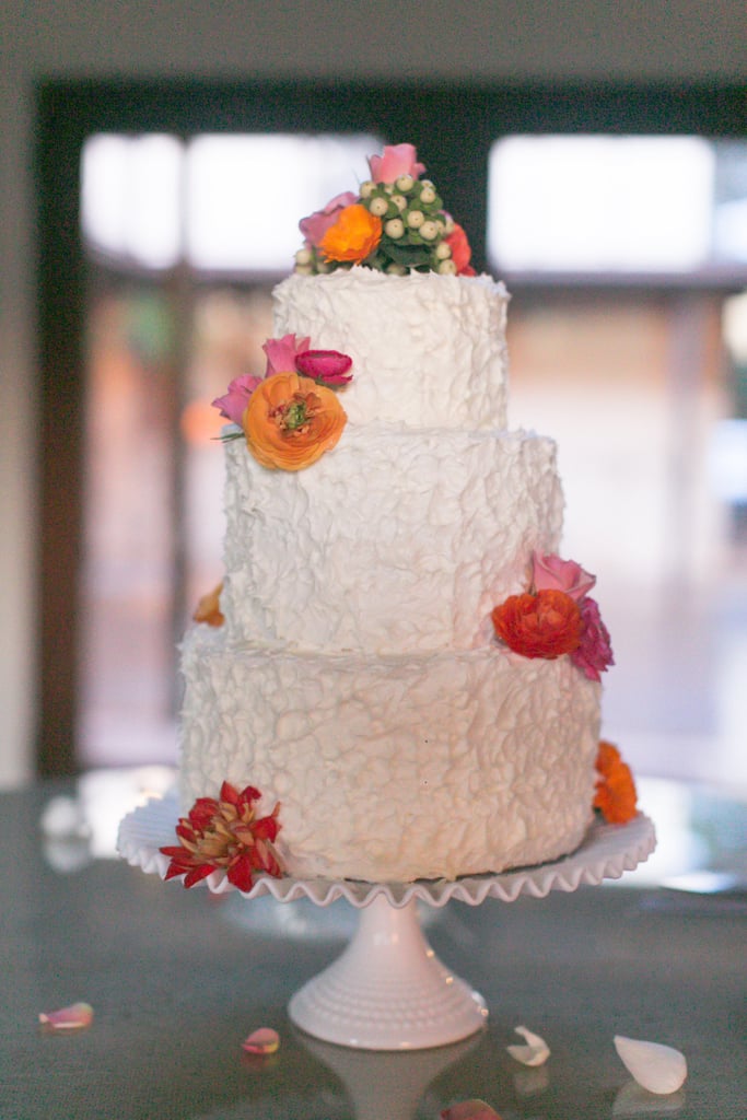 Small bunches of ranunculus, poppies, and dahlias offer color to this white-spackled wedding cake.
